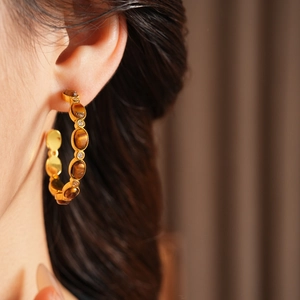 Dettaglio di orecchini vintage a forma di C placcati oro con occhio di tigre e zirconi