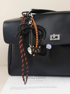 Detail of handmade heart and bow bag charms with a cat plush on a leather handbag