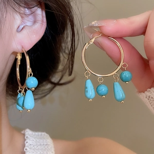 Detail of bohemian gold hoop earrings with turquoise teardrop beads on a model