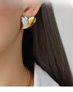 Gros plan de boucles d'oreilles cœur bicolores dorées et argentées portées par un mannequin