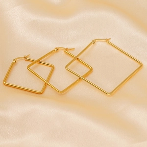 Three pairs of golden square hoop earrings in different sizes on silk fabric