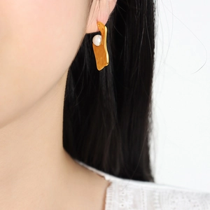 Boucles d'oreilles dorées irrégulières avec perle blanche portées par modèle