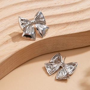 Detail shot of silver ribbon bow stud earrings with intricate metallic texture folds