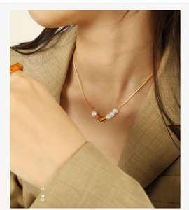 Détail d'un collier cœur doré élégant avec perles blanches sur un blazer kaki