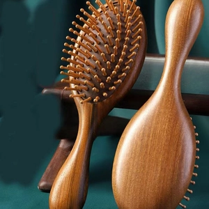 Deep brown sandalwood massage hairbrush with 28 wooden teeth on dark green fabric