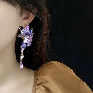 Detail of purple flower earrings with rhinestones and teardrop crystals on a black background