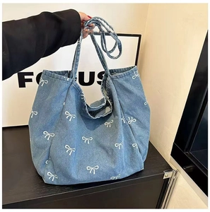 Detailed view of large denim tote bag featuring white bow prints and shoulder straps