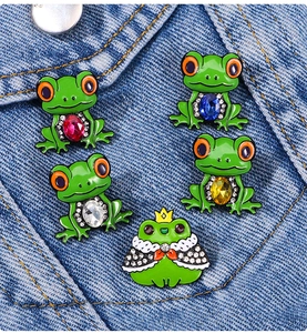 Detail of cute enamel frog pins with colorful gemstones on dark blue denim fabric