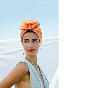 Detailed close-up of vibrant orange fashion turban with gold earrings and metal necklace