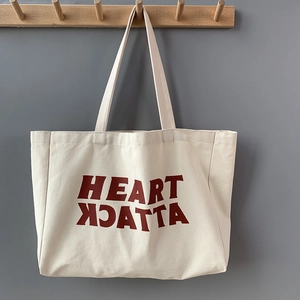 Detail of off-white canvas tote bag with red HEART ATTACK print on a wooden hook