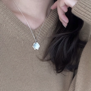 Detail of a 925 silver bamboo necklace with a blue shell pendant worn on a brown sweater