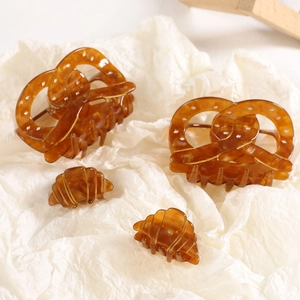 Détail de pinces à cheveux en acétate ambré aux formes de bretzel et croissant sur papier