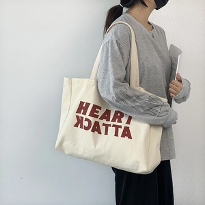 Detail of a large cream canvas tote bag with red Heart Attack print on a female model