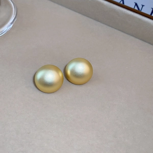 Detail view of round matte gold earrings with minimalist textured button design on display