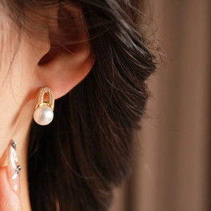 Gros plan de boucles d'oreilles dorées en U avec zircon et perle blanche pendante