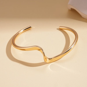 Macro view of golden wavy irregular geometric open cuff bracelet with metallic finish