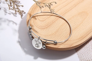 Detail of silver adjustable steel bracelet with cartoon girl charm on a wooden tray