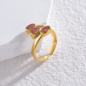Detail of gold open ring with three oval pink gemstones on a white textured stone