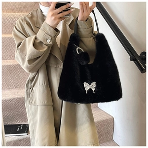 Detail of black faux fur shoulder bag with silver butterfly charm and plush pompom pendant