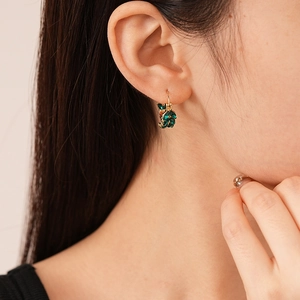 Detail shot of vintage leaf-shaped gold earrings with emerald green zircon on ear