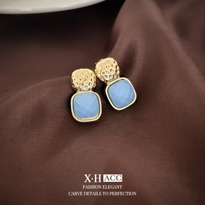 Close-up of gold square earrings with blue gems on brown silk fabric with text