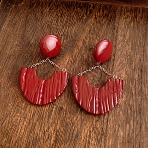 Macro detail of red resin U-shaped earrings with unique pleat textures on wood surface