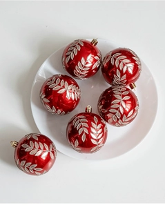 Dettaglio palline di Natale rosse con motivi a foglie d'argento su un piatto bianco