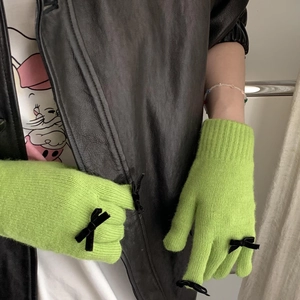 Detail of neon green knit gloves with black bows shown on model wearing black leather jacket