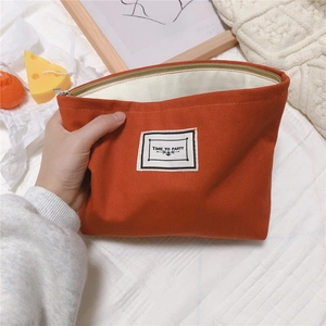 Detail of orange houndstooth canvas pouch with white fabric label and zipper closure