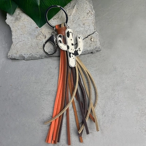 Cow print cactus keychain with colorful leather tassels on a rustic concrete background