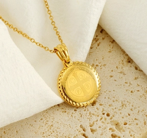 Macro view of gold Saint Benedict medallion necklace on textured stone and linen