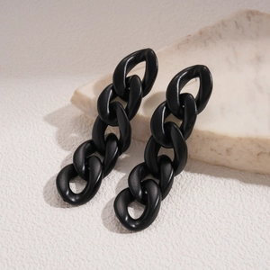 Close-up of black acrylic chain link earrings on a textured stone for a dark aesthetic