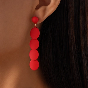 Close-up of model wearing matte red geometric earrings with four circular dangling discs