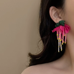 Pink fabric flower earrings with long beaded tassels on model against warm background