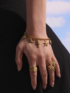 Gros plan d'un bracelet à breloques océaniques dorées et de bagues solaires portées