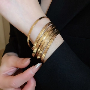 Detail of stacked gold bangles with LOVE engraving and textured patterns on model