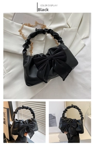 Detail view of black pleated PU handbag with a large satin bow and gold chain strap