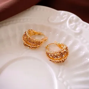 Elegant gold-plated C-shaped hoop earrings with amber crystals on a vintage ceramic plate
