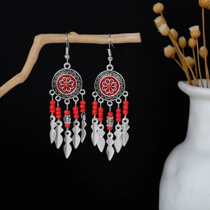 Detail of bohemian drop earrings with red beads and leaf pendants on a wooden branch