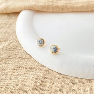 Detailed macro view of gold plated round studs with white marble stone on a tray
