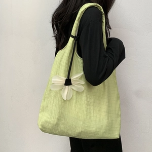 Detail of light green pleated fabric tote bag featuring a minimalist white flower charm