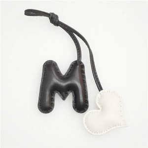 Detail view of handmade leather bag charm featuring a stitched M-letter and white heart