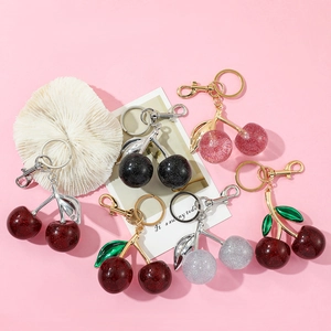 Detail shot of glittering cherry keychains in multiple colors on a soft pink background
