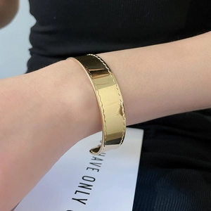 Detailansicht eines goldfarbenen, glänzenden, offenen Armreifs mit Wellenschliffkanten.