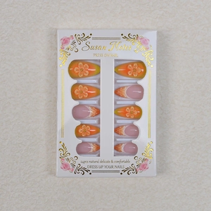 Detailed view of almond-shaped press-on nails with gradient orange flowers and gold beads