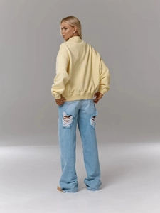 Détail arrière d'un sweat-shirt ample jaune clair et d'un jean bleu clair avec déchirures
