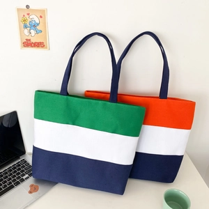 Detailed view of color-blocked canvas tote bags in green, orange, white and navy blue
