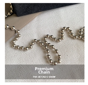 Macro shot of silver metal ball chain strap with high-gloss finish on dark fabric