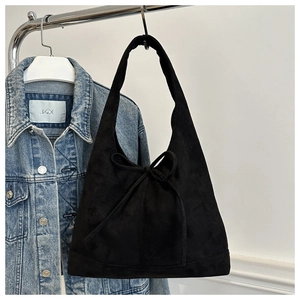 Detail of black suede shoulder bag with bow ornament hanging on a rack with denim jacket