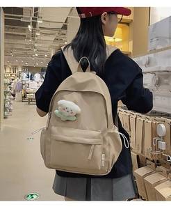 Close-up of beige waterproof backpack with fashion label and white floral plush charm